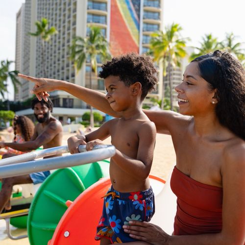 Happy family on aqua-cycle water trike at Waikiki Beach with Hilton Hawaiian Village Rainbow Tower behind