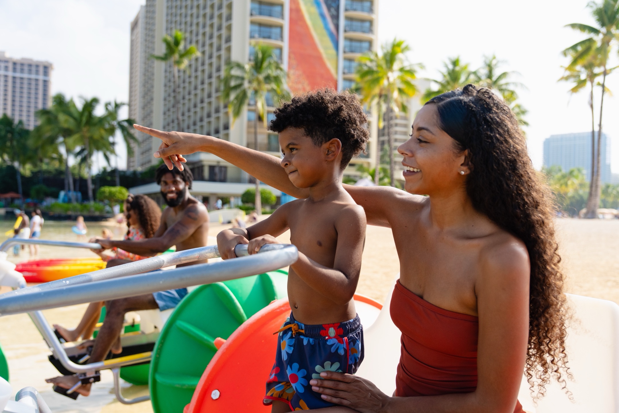 Happy family on aqua-cycle water trike at Waikiki Beach with Hilton Hawaiian Village Rainbow Tower behind