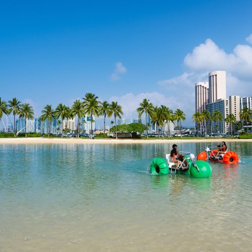 Colorful aqua-cycle water trikes in Waikiki lagoon with palm trees and Hilton Hawaiian Village beach
