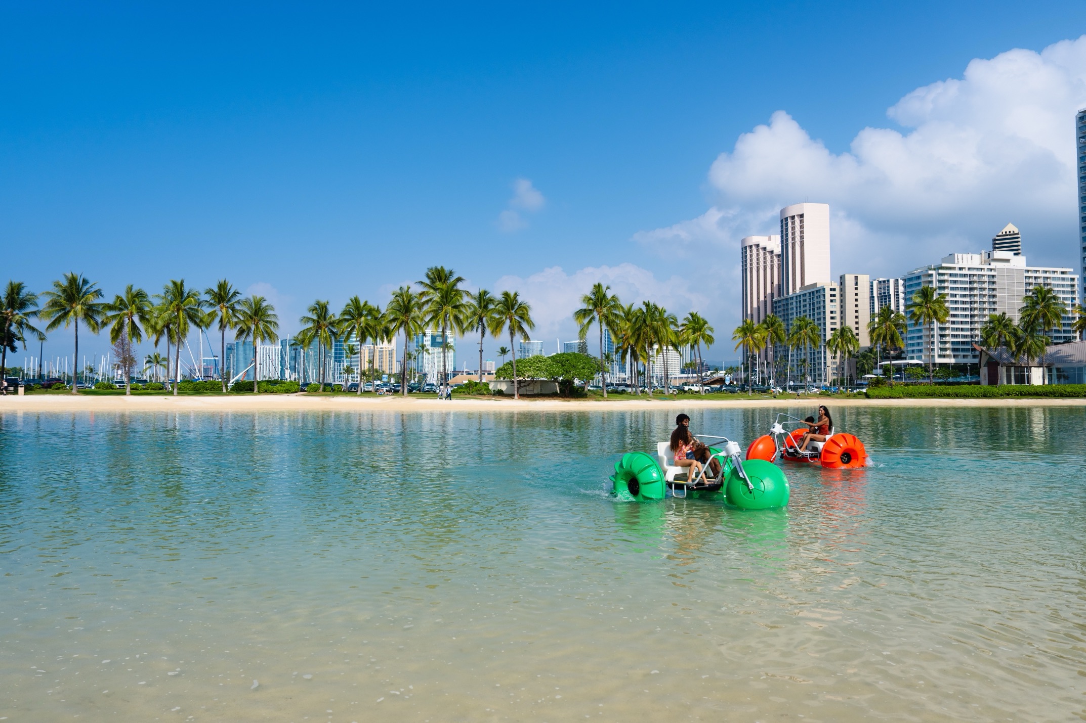 Colorful aqua-cycle water trikes in Waikiki lagoon with palm trees and Hilton Hawaiian Village beach