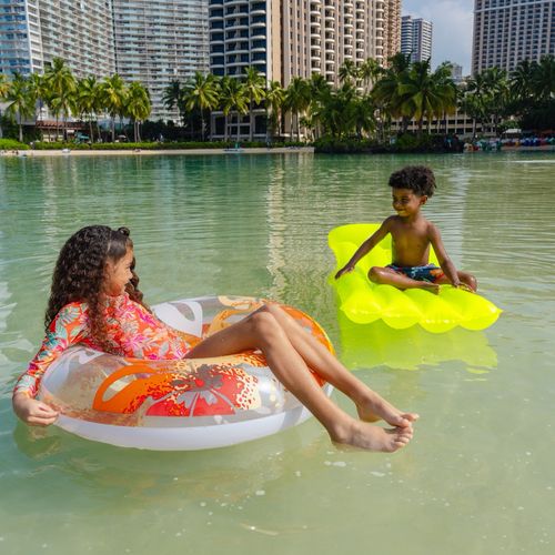 Children floating on colorful pool tubes in Waikiki lagoon with Hilton Hawaiian Village resort in background