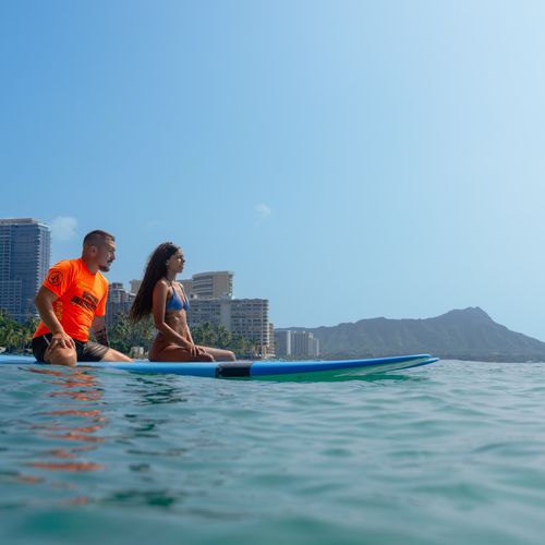 Surf instructor and student sitting on longboards in Waikiki waters with Diamond Head crater in background