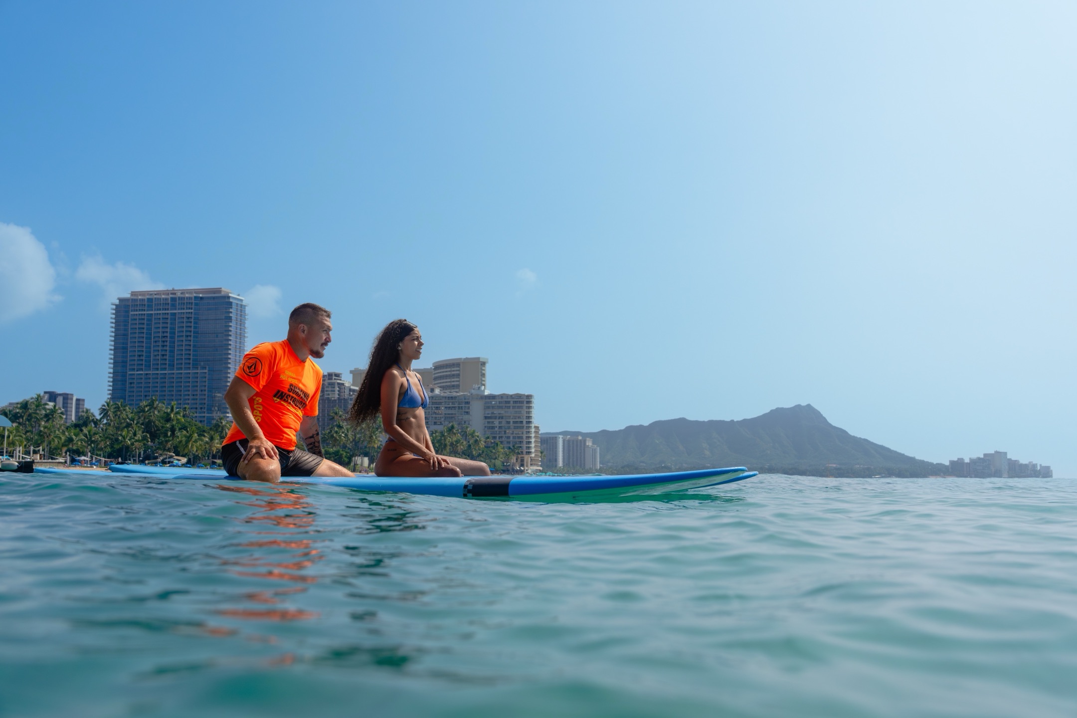 Surf instructor and student sitting on longboards in Waikiki waters with Diamond Head crater in background